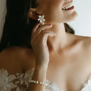 Close-up of a smiling bride wearing the Fleur de Perle floral cluster pearl earrings with a lace wedding dress and veil.