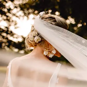 Back view of a blonde bride with a sweeping tulle veil wearing the Grand Jardin white and gold statement floral cluster earrings.